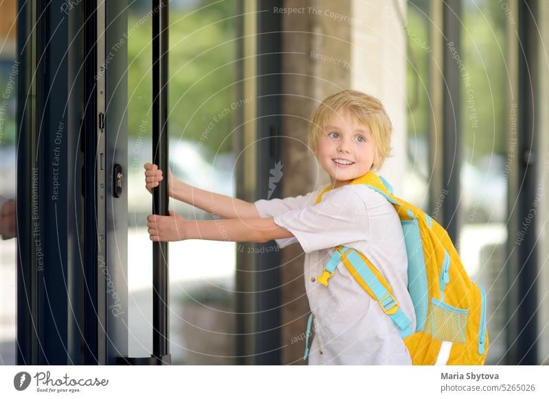 Little schoolboy leaves the house to go to school after holiday. Child in a yard of schoolhouse. Quality education for children. Kids back to school door kids