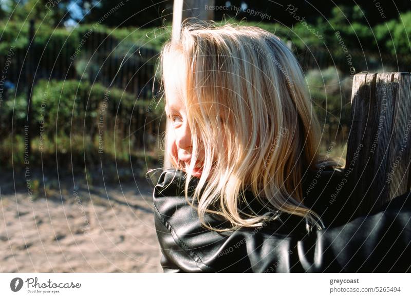 Little girl climbing fence on sunny day kid countryside funny having fun rural childhood cheerful smile leather jacket nature style enjoy positive blond happy