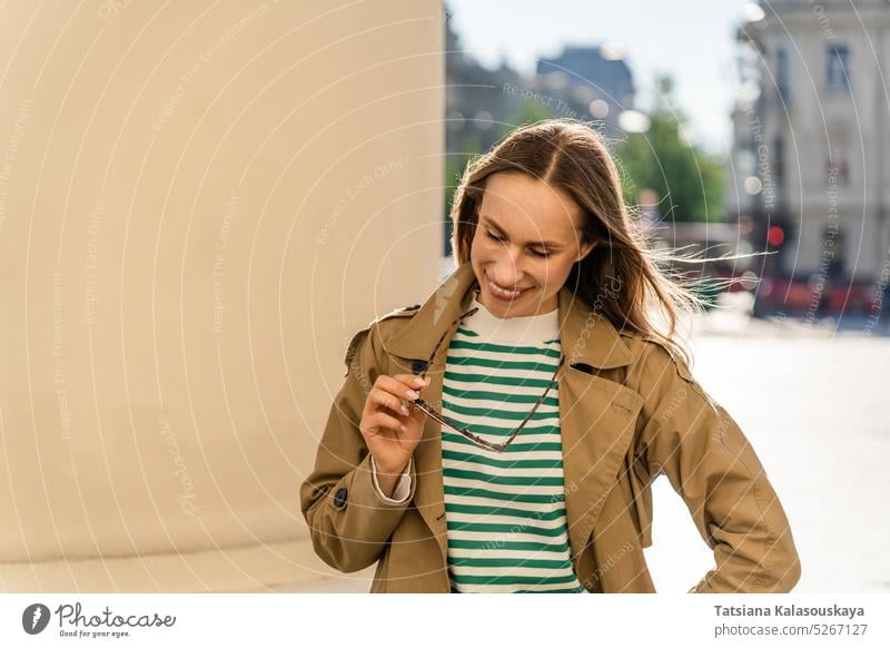 A woman smiles and holds sunglasses while walking in the city happy happiness female cheerful joy adult midlife long-haired dark hair Attractive toothy smile