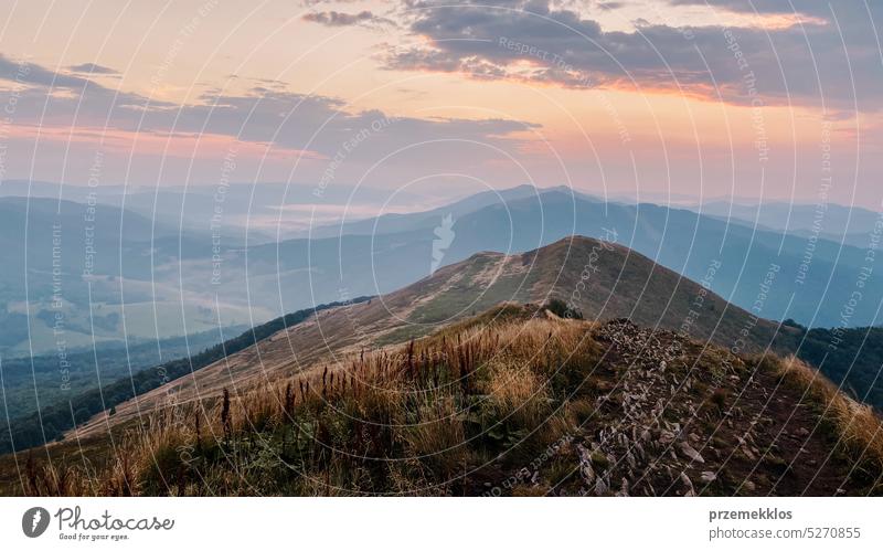 Sunset in mountains. Natural mountain landscape with illuminated misty peaks, foggy slopes and valleys, blue sky with orange yellow sunlight sunrise sunset