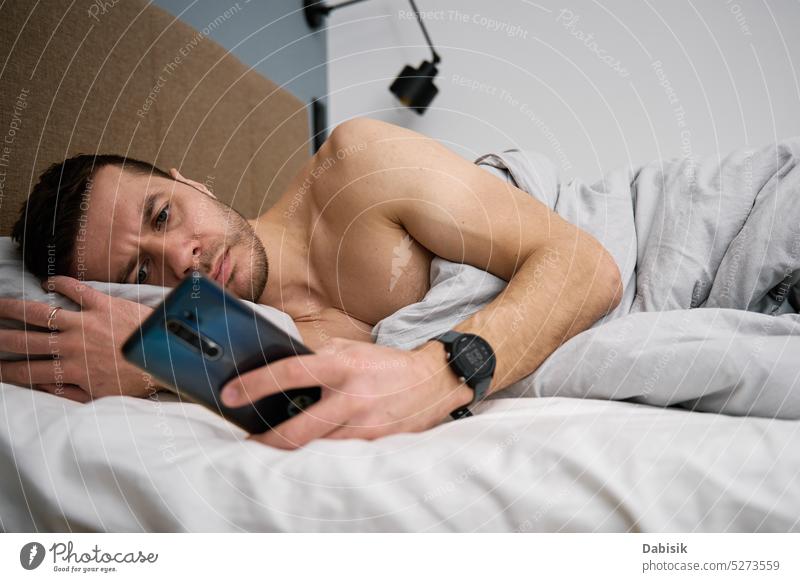 Phone addiction. Man lying in bed with smartphone man bedroom lifestyle browsing morning leisure cellphone online resting blanket technology home concept mobile