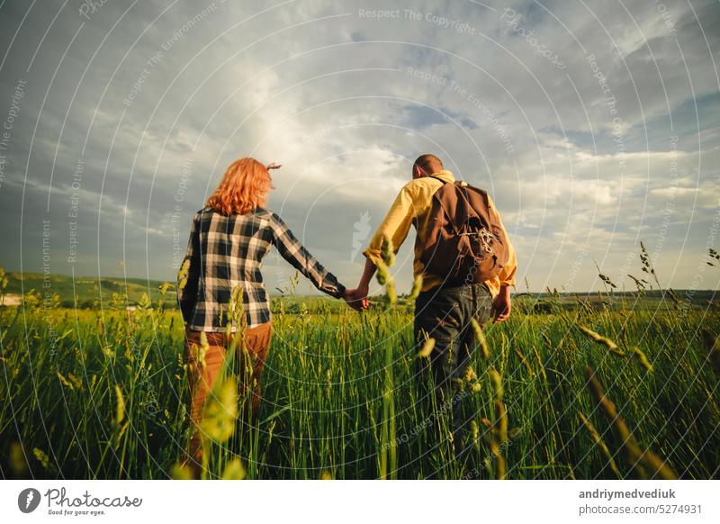 Loving hipster couple walking in the field, kissing and holding hands, hugging, lying in the grass in the summer at sunset. valentines day man love relationship