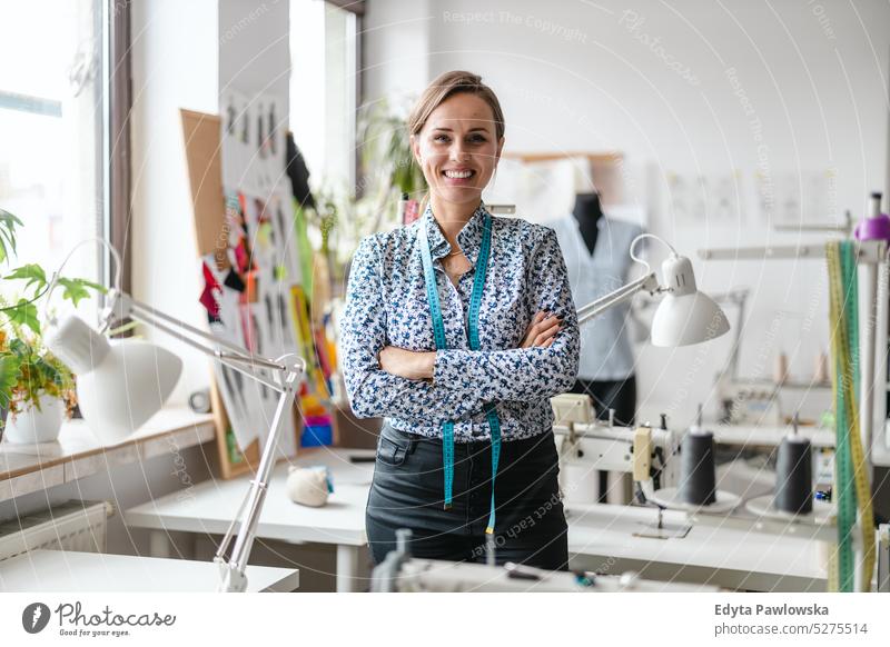 Portrait of young female fashion designer standing at her workplace craft tailoring manufacturing handmade seamstress small business sewing machine workshop