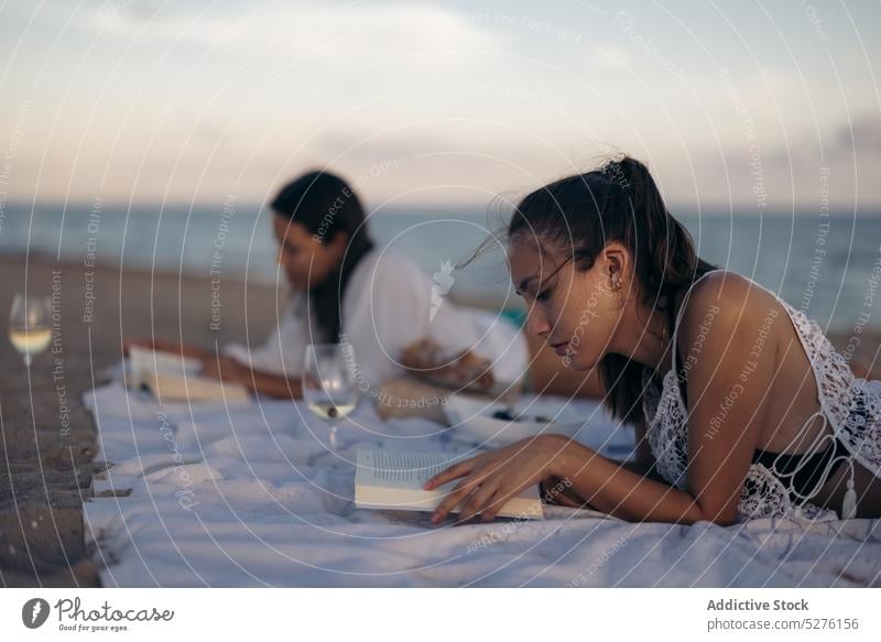 Young women reading books on beach sea sunset weekend blanket vacation together female girlfriend young sand shore coast lying summer lesbian couple lifestyle