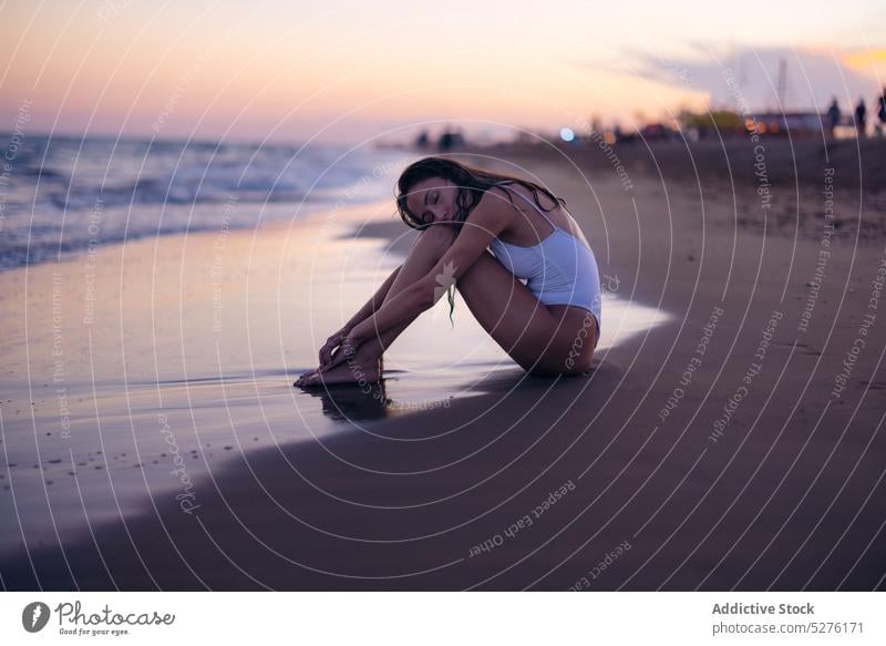 Young female embracing knees on beach woman sea sunset tender love tourist vacation summer resort sundown eyes closed swimwear coast shore ocean sensual calm