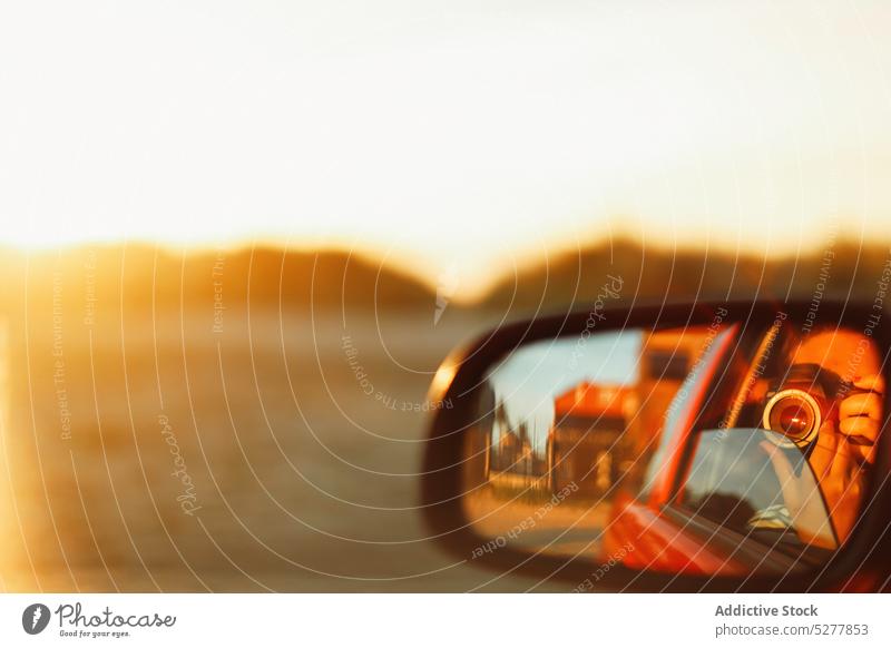 Anonymous traveler with camera in wing mirror car reflection road trip sunshine mountain countryside drive lens photo camera optical sunrise hobby adventure