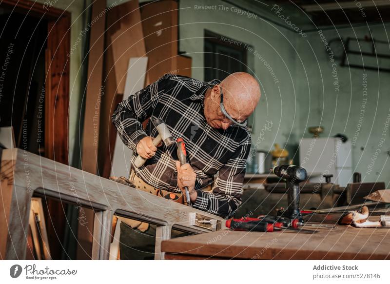 Senior carpenter using chisel and hammer in workshop man woodworker cut craftsman plank skill artisan carpentry male tool instrument equipment process manual