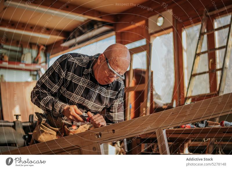 Senior carpenter using chisel in workshop man woodworker cut craftsman plank skill artisan carpentry male tool instrument equipment process manual elderly