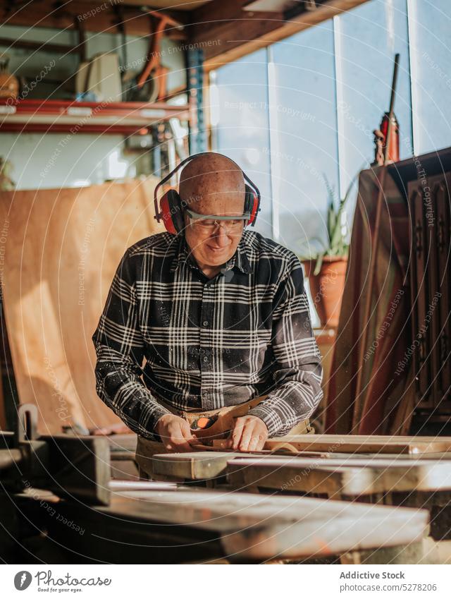 Carpenter cutting wood in workshop man carpenter woodwork wooden carpentry joinery plank professional headphones equipment woodworker male artisan skill tool