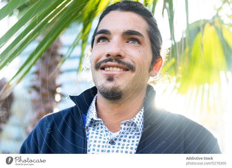 Smiling ethnic man looking away in green park plant positive nature admire glance human face leaf confident appearance charismatic male adult hispanic brunet