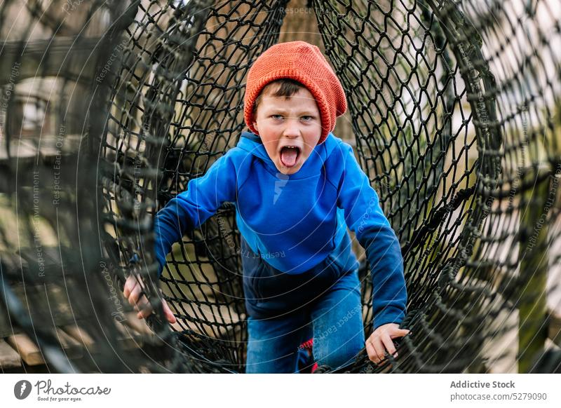 Funny boy climbing on net in park playground playful joy having fun amusement weekend kid child childhood activity happy pastime cheerful game smile preschool