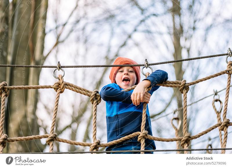 Smiling boy climbing on net on playground park autumn rope pastime weekend amusement child kid happy cheerful activity smile joy playful fun positive childhood