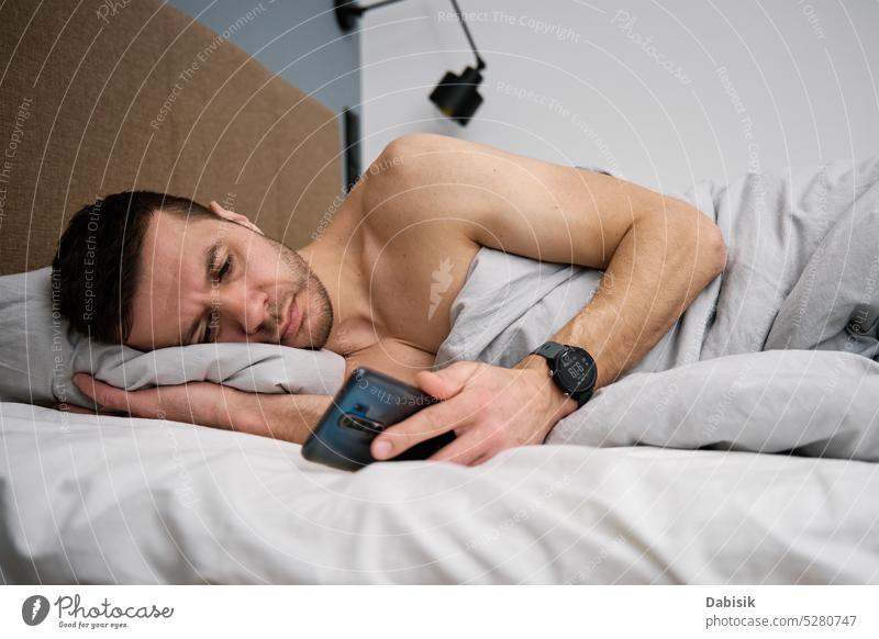 Phone addiction. Man lying in bed with smartphone man bedroom lifestyle browsing morning leisure cellphone online resting blanket technology home concept mobile