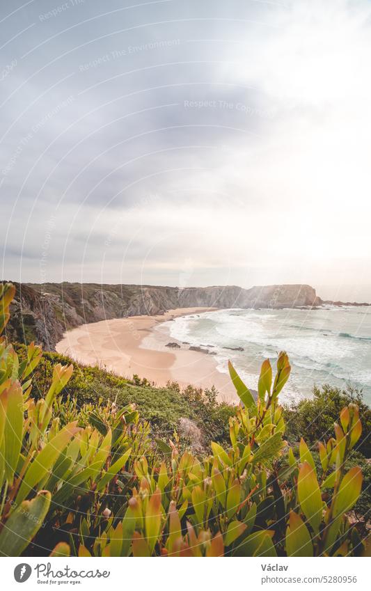 Famous Praia dos Machados beach in Odemira, western Portugal. The rocks surrounding the moon-shaped sandy beach with large waves from the Atlantic Ocean. Fisherman Trail