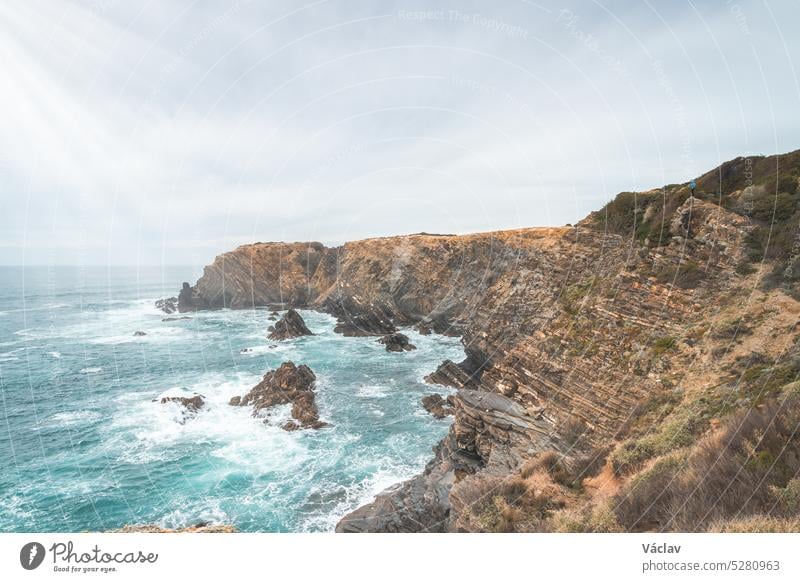 Hiker stands on rugged rock and cliff coastline on the Atlantic Ocean near the town of Odeceixe in the west of Portugal in the famous tourist region of the Algarve. Sunset