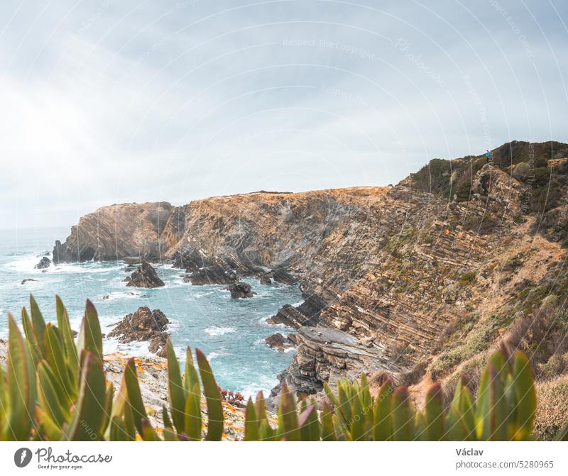 Hiker stands on rugged rock and cliff coastline on the Atlantic Ocean near the town of Odeceixe in the west of Portugal in the famous tourist region of the Algarve. Sunset