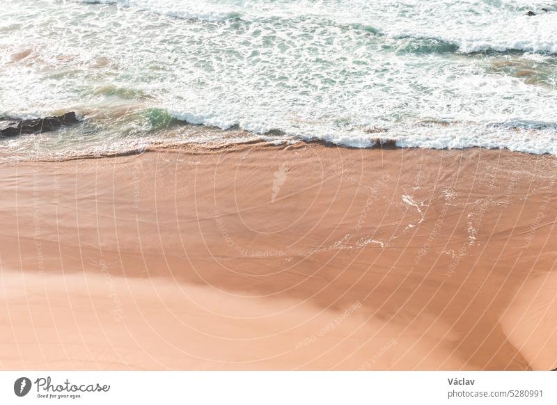 Gentle flow of blue-green waves on a yellow sandy beach in the Odemira region, western Portugal. Wandering along the Fisherman Trail, Rota Vicentina