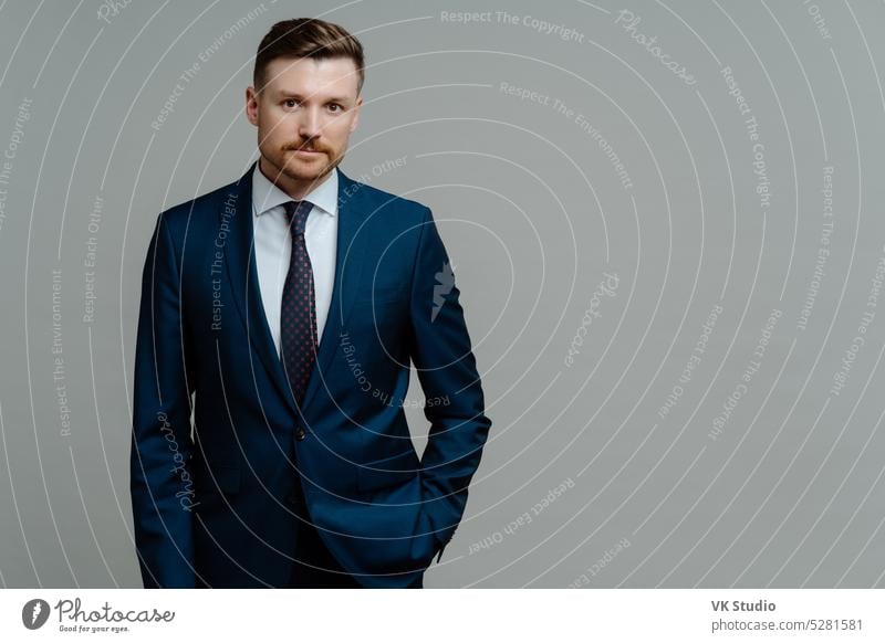 Confident male boss in blue navy suit looking at camera while standing against grey background young successful businessman leader formal office confidence