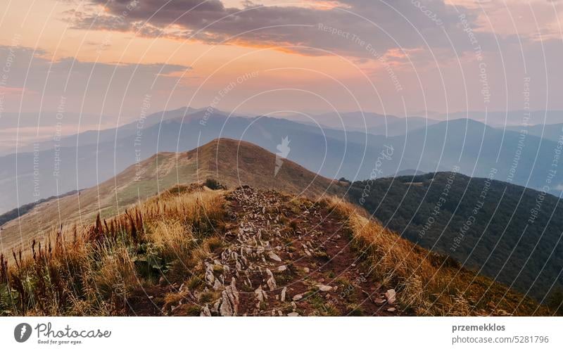 Sunset in mountains. Natural mountain landscape with illuminated misty peaks, foggy slopes and valleys, blue sky with orange yellow sunlight sunrise sunset