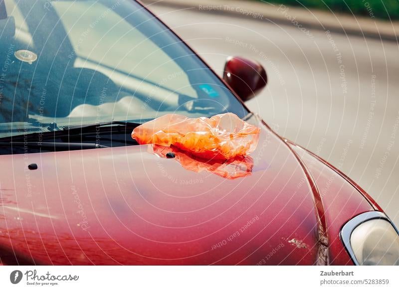 Orange plastic bag on hood of red car Red Car Hood Plastic bag Trash Town Mobility Climate Environment Past Oil Swing Line Aesthetics splendour Problem