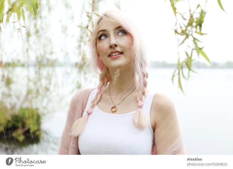 Young woman with pink blonde hair looks at sky and smiles in front of lake with lakeside in distance Woman portrait pretty Slim long hairs pink hair Pink Blonde