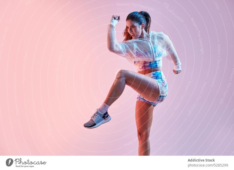 Stylish sportswoman jumping on pink background athlete active fitness style sportswear activewear energy colorful studio shot young female slim arm raised