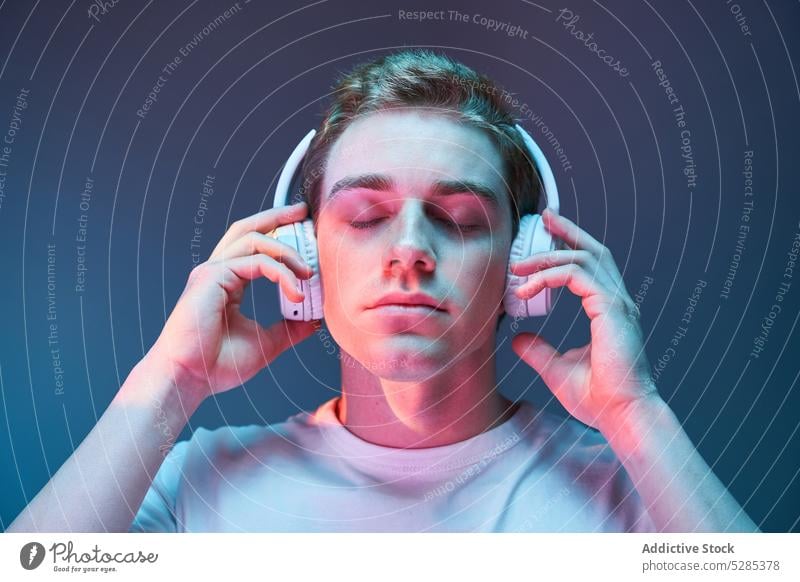 Man listening to music in headphones man neon relax wireless calm illuminate eyes closed male young sound song modern audio casual glow gadget device cool