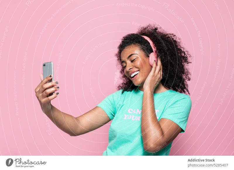 Delighted black woman taking selfie on smartphone music listen headphones smile happy cheerful eyes closed african american female young ethnic device gadget