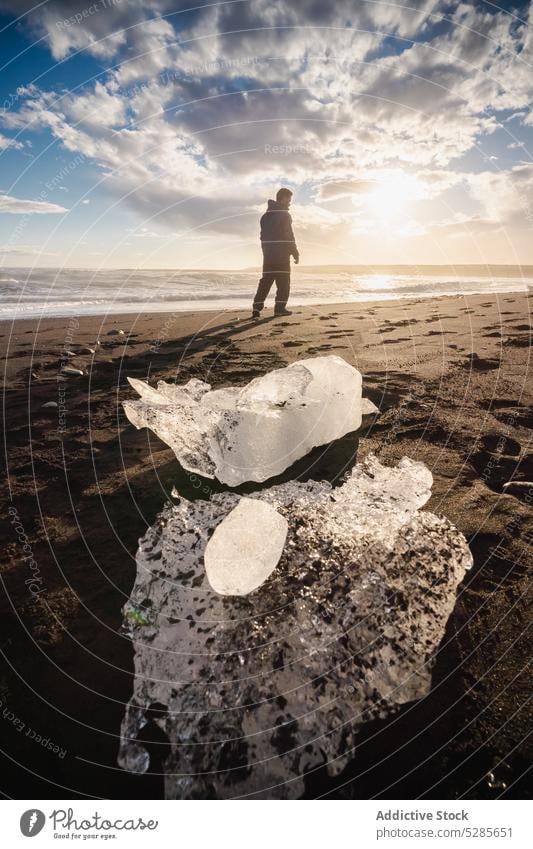 Anonymous traveler on seashore with ice chunks in sunlight tourist frost journey cloudy weather cold coast frozen silhouette sky iceland trip peaceful explore