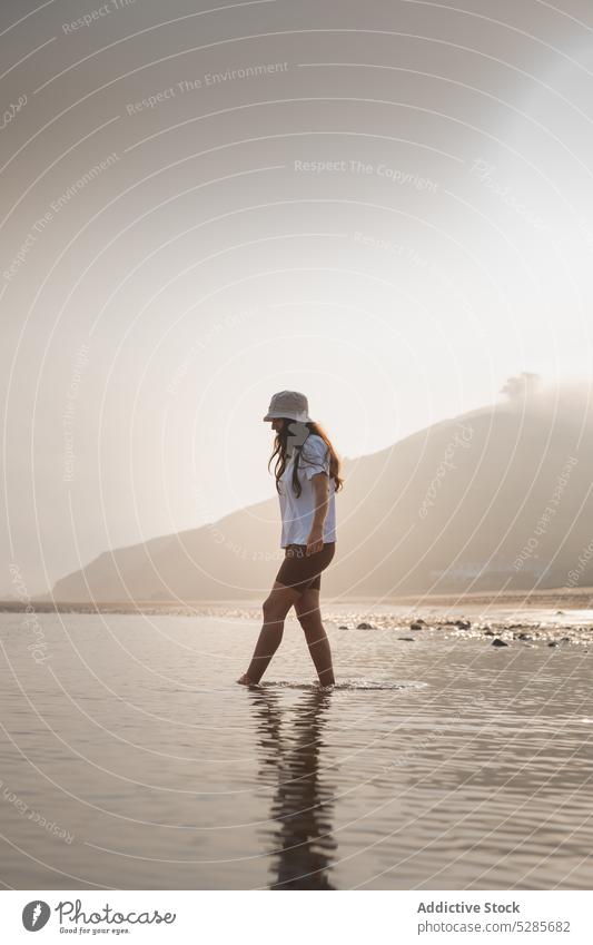 Woman walking in sea water near mountain woman tourist shore beach summer vacation nature coast spain asturias hat ocean sun seashore female sky seaside