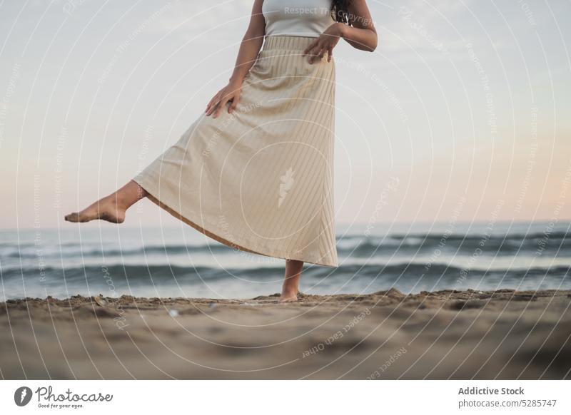 Anonymous carefree young Hispanic lady kicking sand on seashore woman beach leg raised ocean enjoy vacation sunset tourist happy female hispanic ethnic brunette