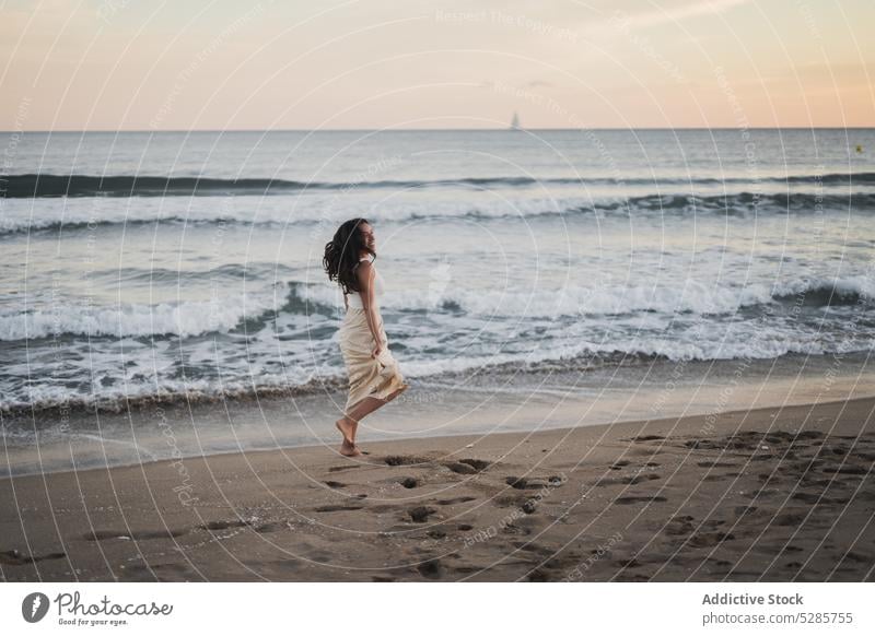 Cheerful young ethnic woman walking on sandy seashore during summer vacation beach smile enjoy happy holiday sunset traveler nature female hispanic barefoot