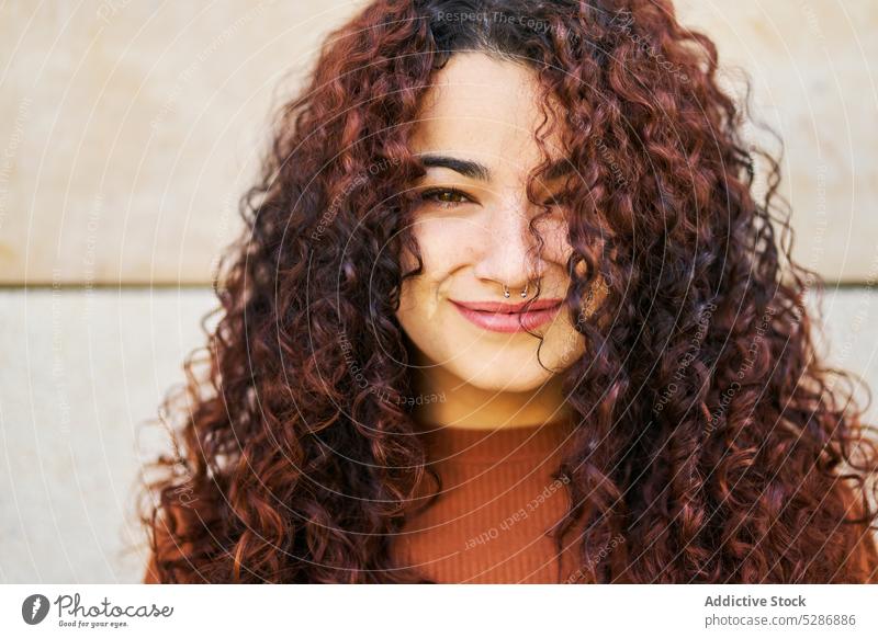 Happy woman standing against wall and smiling smile happy curly hair cheerful warm clothes positive trendy walk joy female modern glad charming city lifestyle