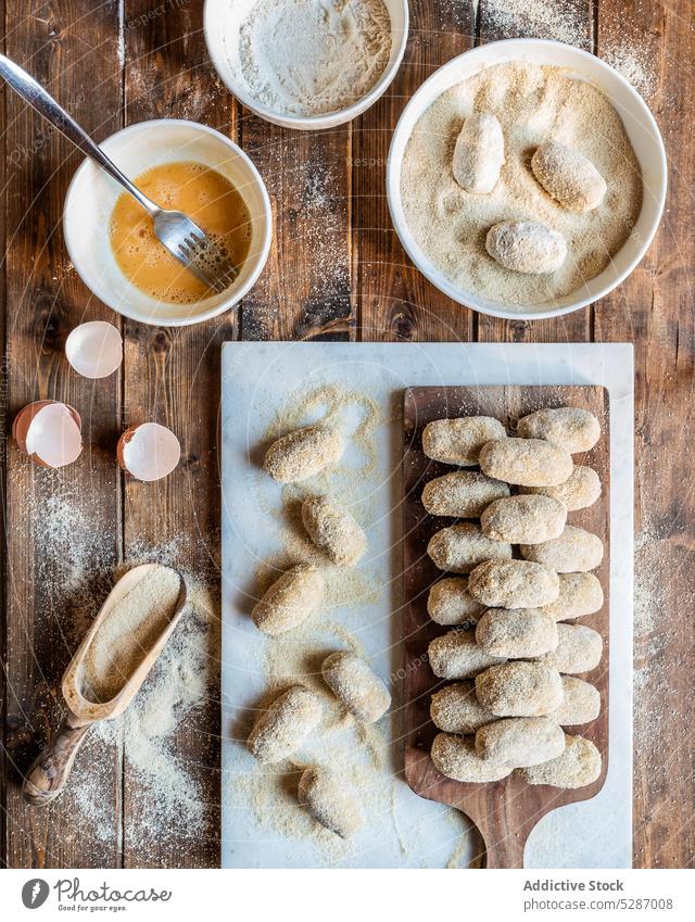 Uncooked pork cheeks croquettes placed on wooden table process uncooked egg bread crumb bowl ingredient culinary kitchen food cutting board prepare cuisine