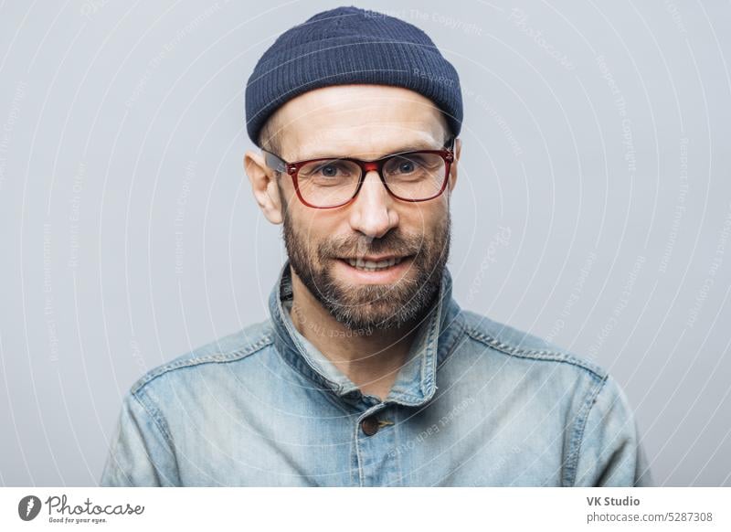 Indoor shot of handsome unshaven male with satisfied expression, rejoices achieving success at work, looks happily through spectacles, isolated over white background. Smiling bearded man indoor