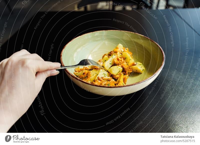 A woman dines on a fresh, vegetarian seasonal lunch. Fried wild mushrooms, chanterelles with boiled potatoes and herbs green parsley dill bowl table hand fork