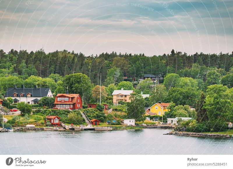 Sweden. Beautiful Red And Yellow Swedish Wooden Log Cabins Houses On Rocky Island Coast In Summer Evening. Lake Or River Landscape. sweden house huts hygge