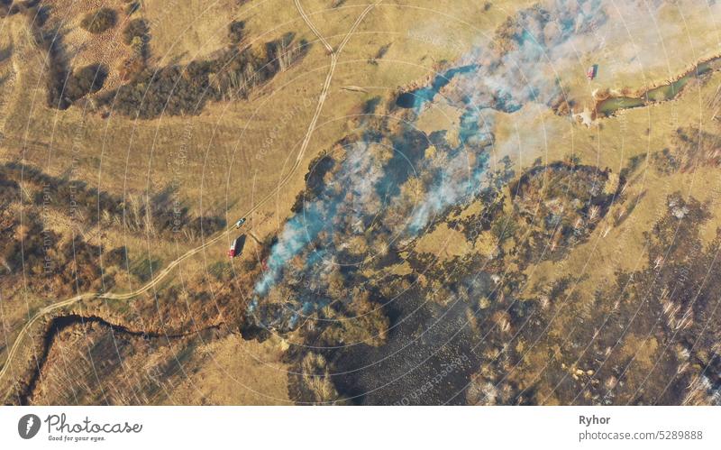 Aerial View. Spring Dry Grass Burns During Drought Hot Weather. Bush Fire And Smoke. Fire Engine, Fire Truck On Firefighting Operation. Wild Open Fire Destroys Grass. Ecological Problem Air Pollution