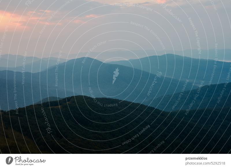 Sunset in mountains. Natural mountain landscape with illuminated misty peaks, foggy slopes and valleys, blue sky with orange yellow sunlight sunrise sunset