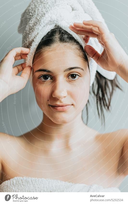 Pretty calm smiley woman with wrap towel on head, enjoys softness of glowing skin and hair treatment. Skincare gel or moisturizer. Relaxed after bath, isolated over grey background.