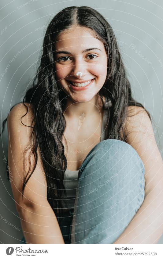 Joyful and funny portrait of a young adult woman with lotion cream on her nose. Skincare, face beauty and woman with cream for acne, dermatology and glow on a studio background.