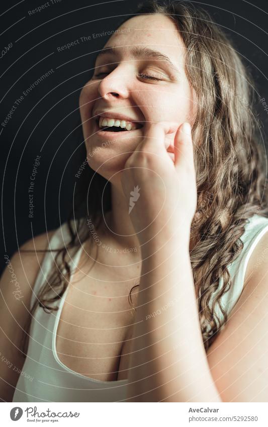 Portrait of a woman smiling and holding her hand to her face posing in a studio with black background. Young adult applies daily care, nourishing facial mask on her skin.