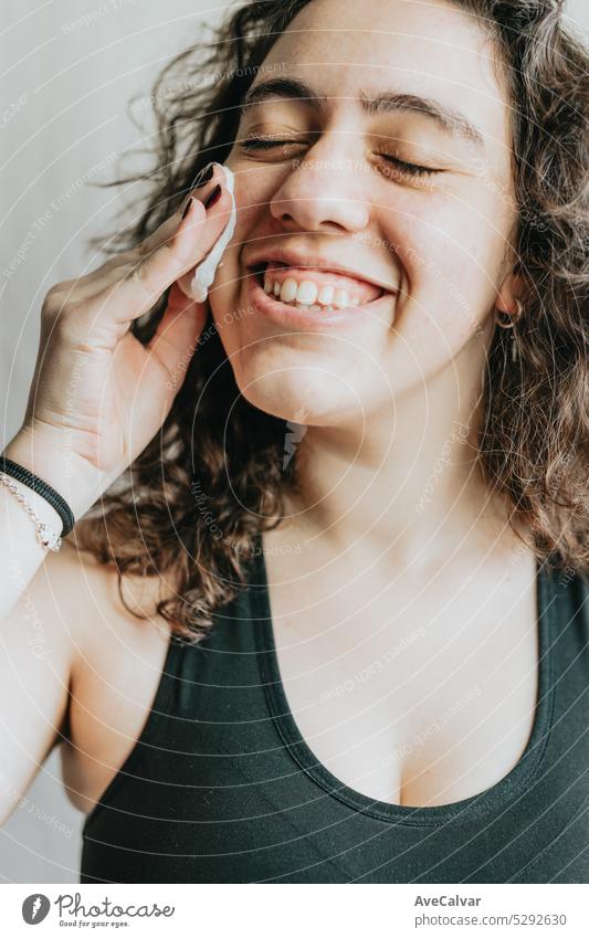 Young woman holding and using cosmetic cotton disc being relaxed and smiling, closeup portrait in studio.Removing cosmetics with hygienic disc. Exfoliating routine before makeup.