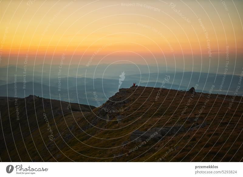 Man looking at sunrise. Mountains at sunrise. Man standing on peak. Natural mountain landscape with illuminated misty peaks, foggy slopes and valleys hiker