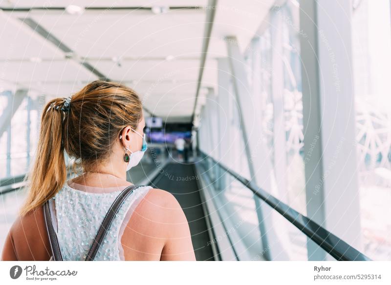 Young woman in mask walks on travolator at shopping mall. Young adult caucasian woman moving on travolator in shopping mall. Young woman in mask walks on travolator at shopping mall. Young adult caucasian woman moving on travolator in shopping mall