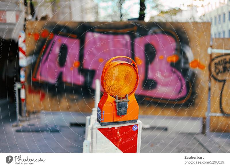 Orange warning light on road limiter in front of pink graffiti on construction fence Warning light warning board Road delimiter Graffiti Street art Hoarding