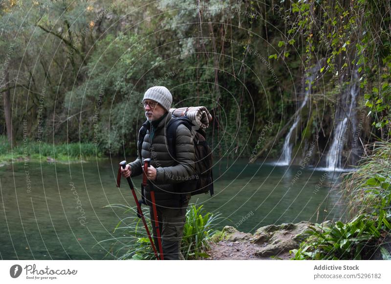 Man with backpack walking with trekking poles man forest hiker woods lake explore nature adventure male traveler trip elderly wanderlust tourism waterfall