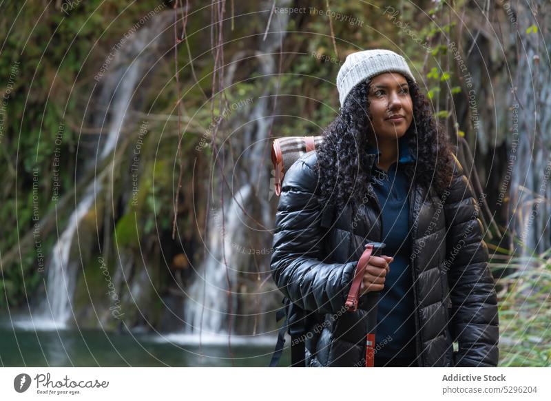 Traveling woman with trekking poles in forest hiker admire waterfall lake nature mountain highland adventure female traveler trip backpack landscape journey