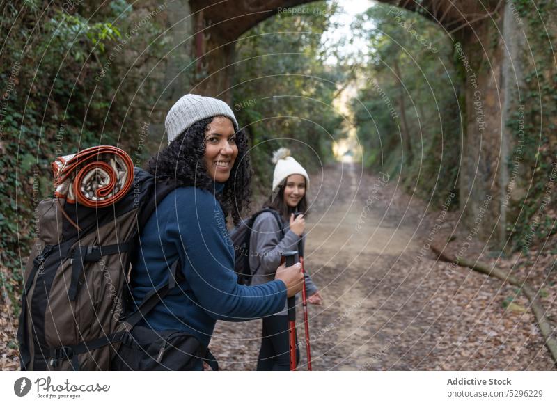 Happy ethnic woman and girl standing in forest mother daughter trekking pathway hike cheerful walk smile nature hiker stroll happy backpack autumn together tree