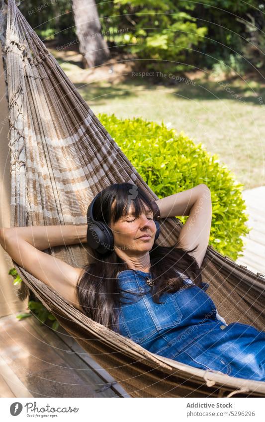 Happy woman listening to music in hammock in park headphones rest yard smile relax leisure song device happy enjoy delight casual audio wireless female positive